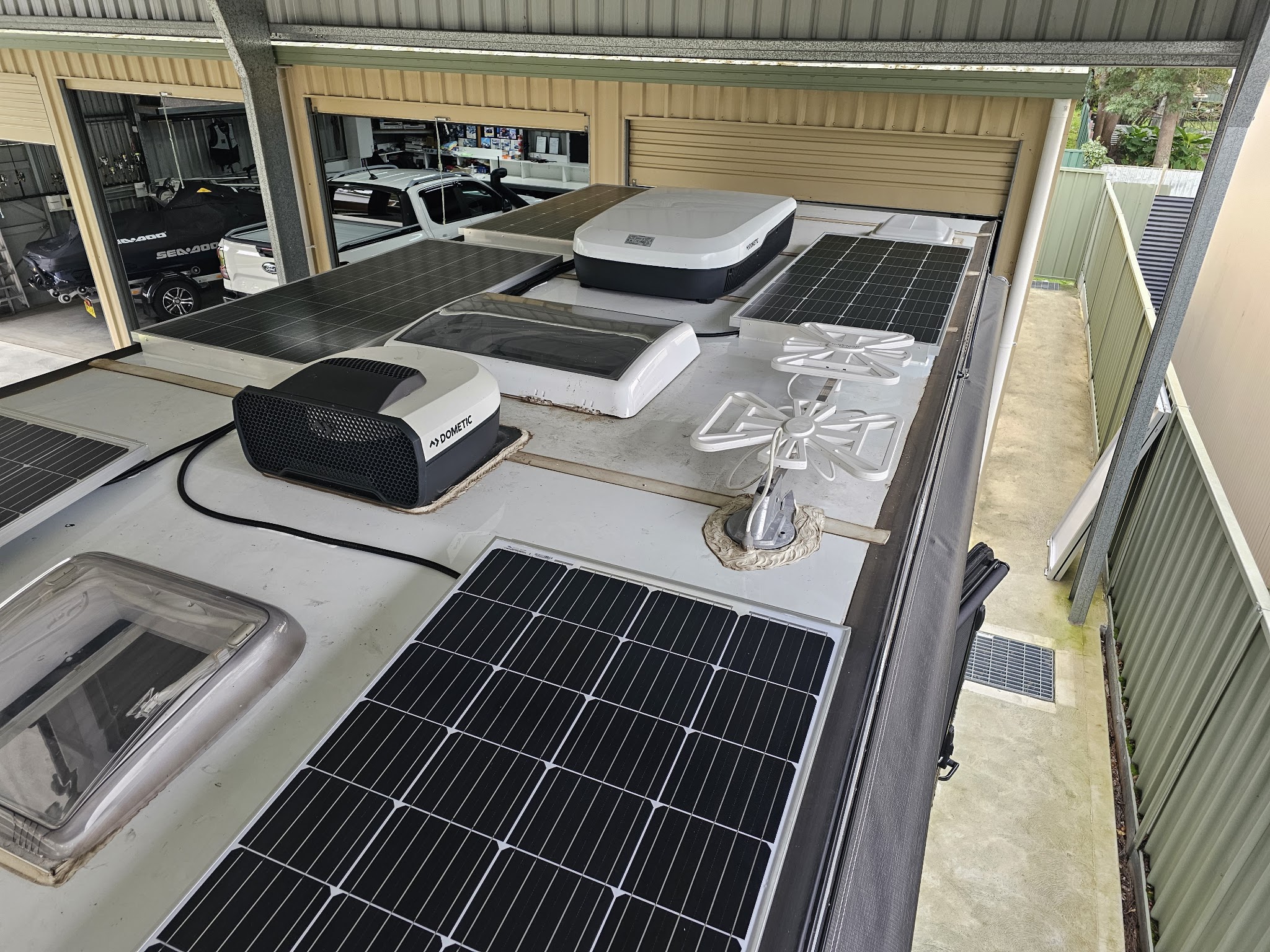 Rooftop solar panels, a Dometic air conditioner and roof vents fitted to a caravan inside a workshop shed